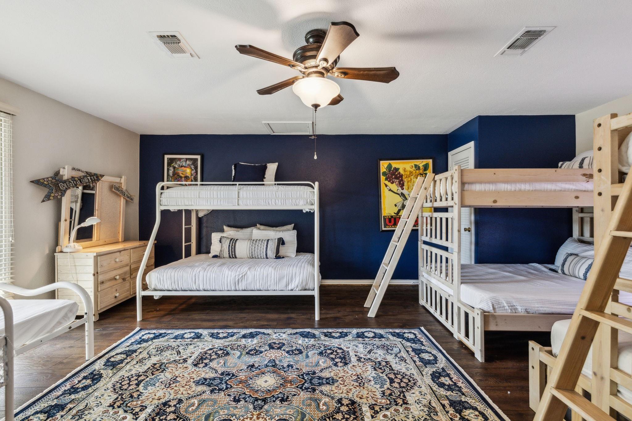 Kids' bunk room with seven beds, navy accent wall, and hardwood floors